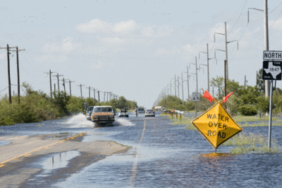 Photo of a flooded road and a sign that says "WATER OVER ROAD".