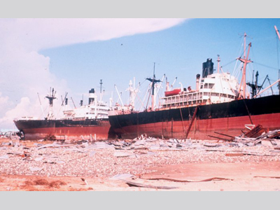 Two large ocean going vessles sitting on dry land amongst debris